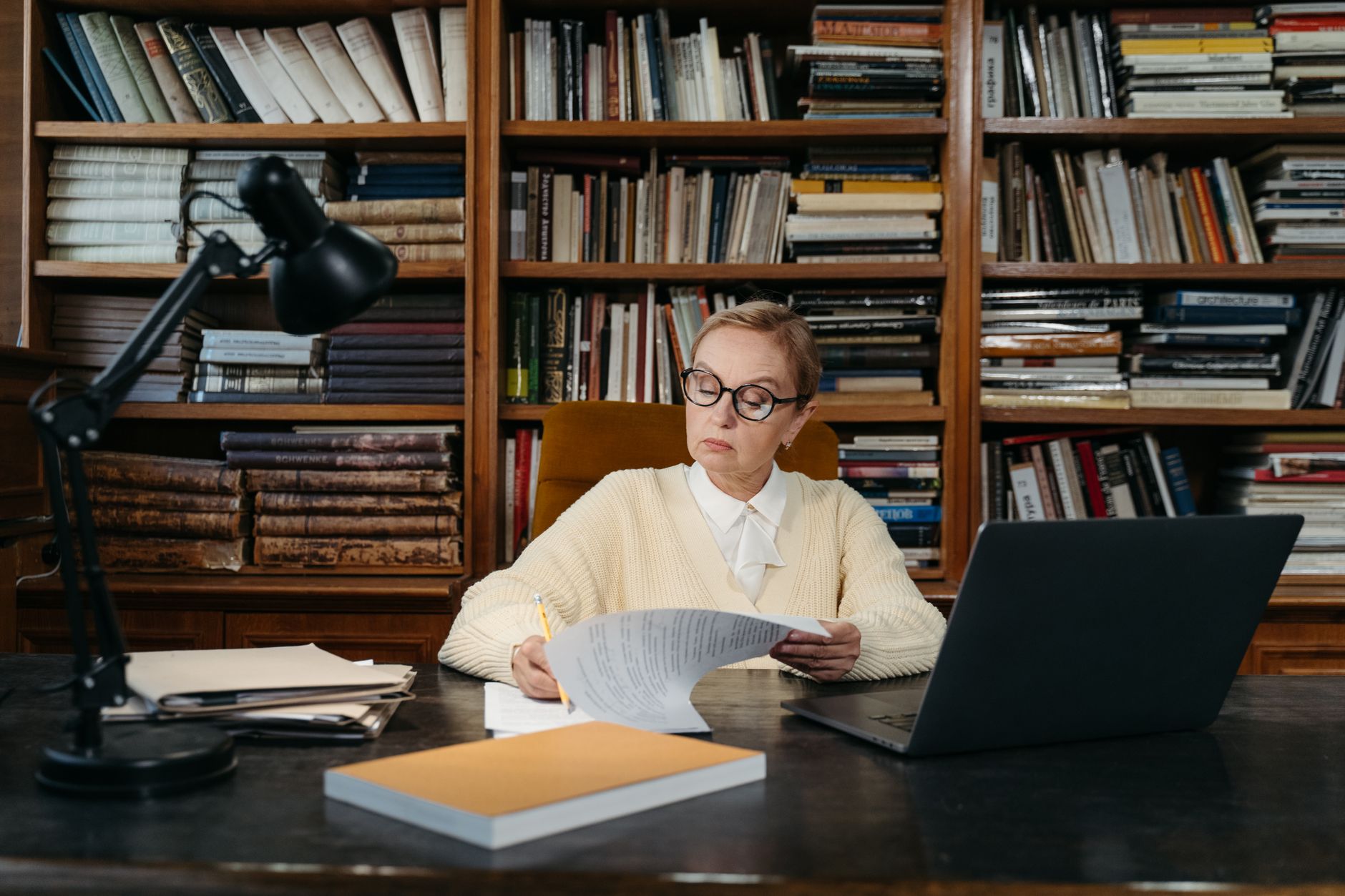 Person prüft am Schreibtisch Unterlagen, im Hintergrund Bücherregale